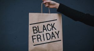 Hand holding a brown paper shopping bag labeled 'BLACK FRIDAY' against a dark blue background.