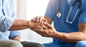 Doctor in blue scrubs gently holds a patient's hand in a comforting gesture in a clinical setting.