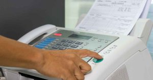 Person pressing the green Start button on a fax/scanner with a printed sheet feeding through the machine