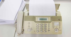 Beige office fax machine with a handset on the left and a stack of paper loaded, ready to print or send.