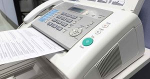 Fax machine with numeric keypad and a printed sheet feeding out of the tray, ready to send or receive a page.