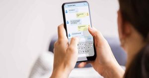 Close-up of hands holding a smartphone displaying a chat conversation with blue and yellow message bubbles and a visible keyboard on screen.